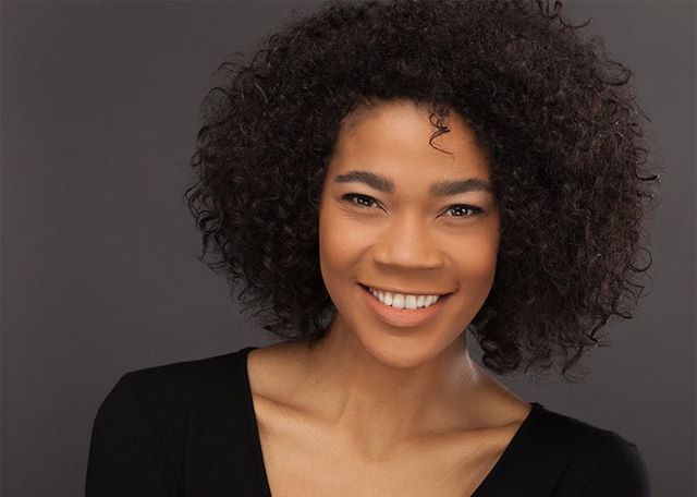A smiling woman with curly hair poses for a studio headshot.