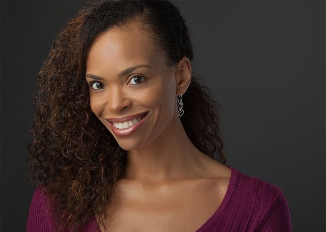 A smiling woman with curly hair poses against a gray background.