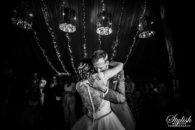 A bride and groom share an intimate first dance at their wedding reception, surrounded by family and friends.