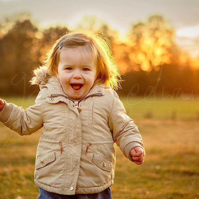 A happy toddler girl plays outdoors at sunset in a field, exuding cheerful energy and joyful childhood moments.