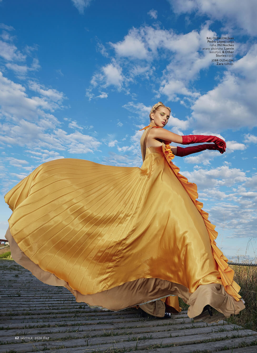 A woman in a yellow dress and red gloves poses in an outdoor editorial fashion shot.