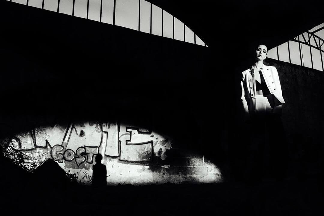 A stylish woman poses in an urban scene with graffiti art, creating a moody, high-contrast image perfect for fashion editorial.