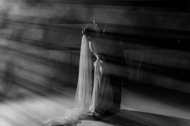 A bride and groom are silhouetted in a dramatic, artistic black and white wedding photograph with strong backlight.