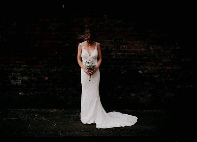 A bride in a white dress holds a bouquet in front of a brick wall on her wedding day.