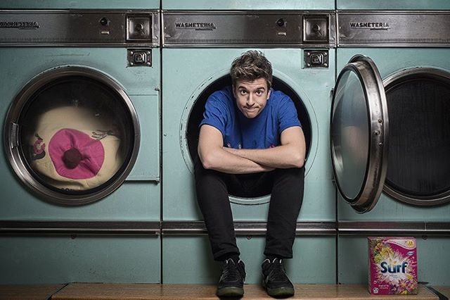 A man sits inside of a washing machine next to a box of Surf laundry detergent.
