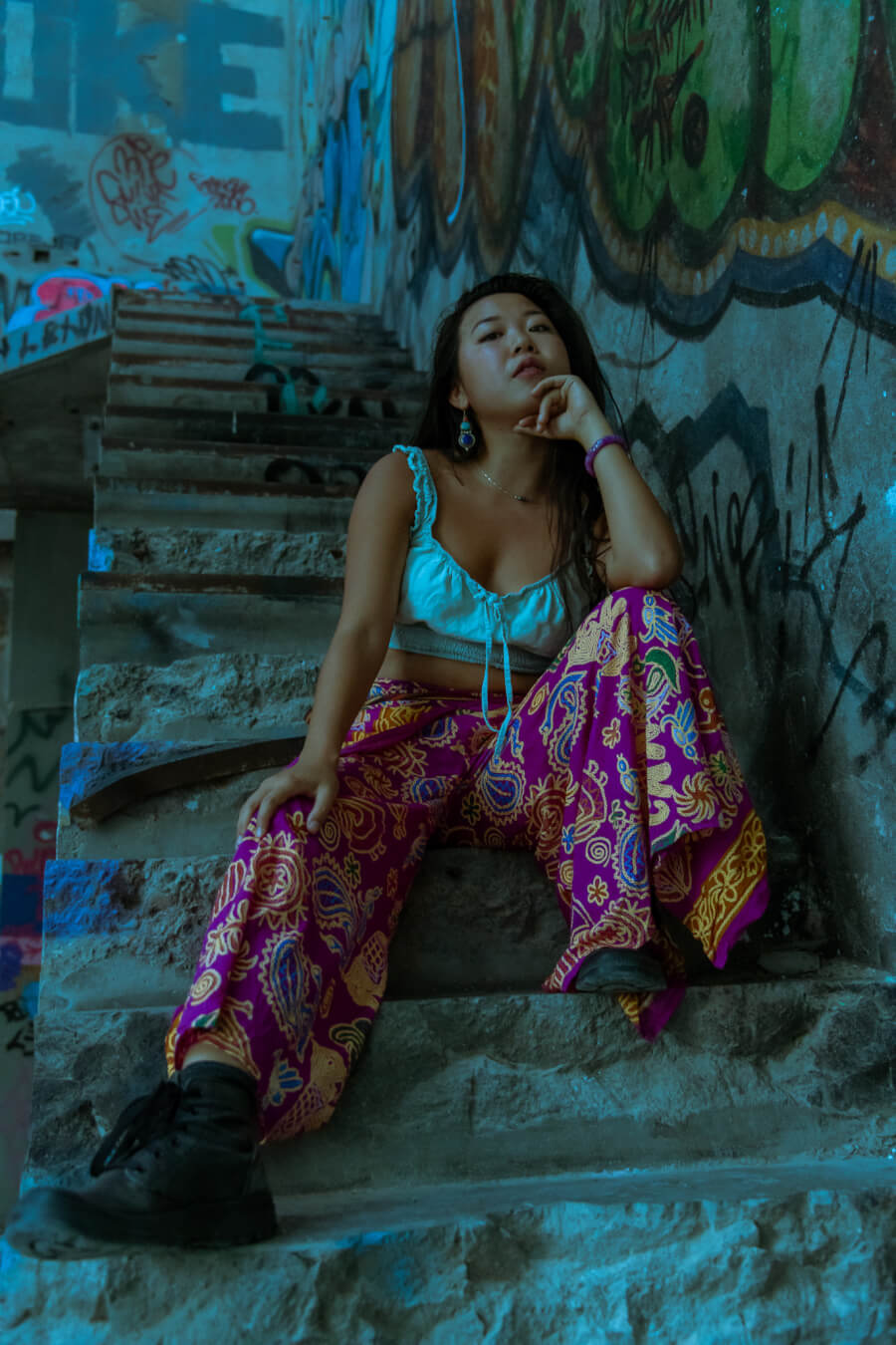 An Asian woman poses on graffiti-covered stairs, showcasing urban fashion in a candid street style portrait.