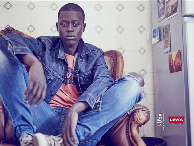 A man in denim sits confidently in a leather chair for a Levi's fashion advertisement.
