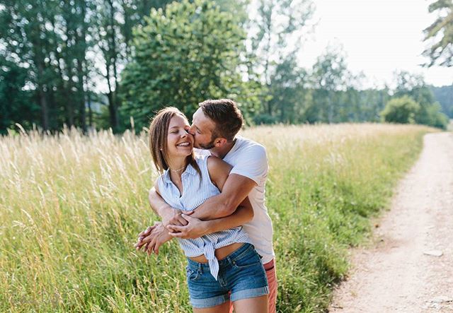 A loving couple embraces in a sunny field, sharing an intimate moment on a nature path.