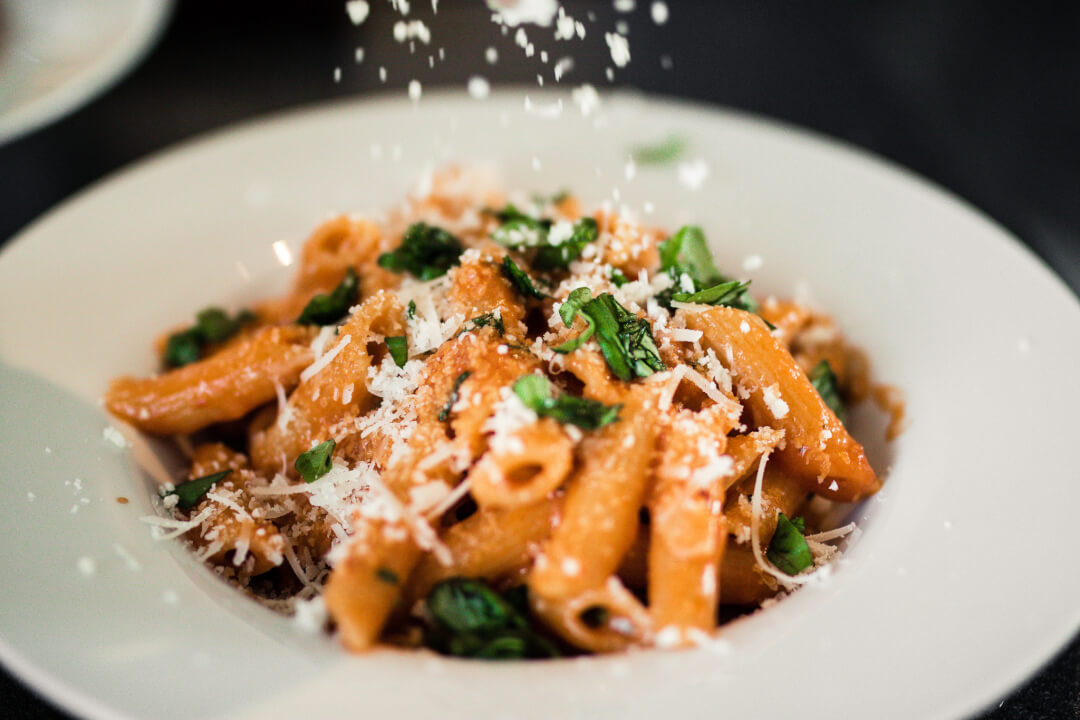 A plate of penne pasta topped with cheese and basil, shot with a shallow depth of field.