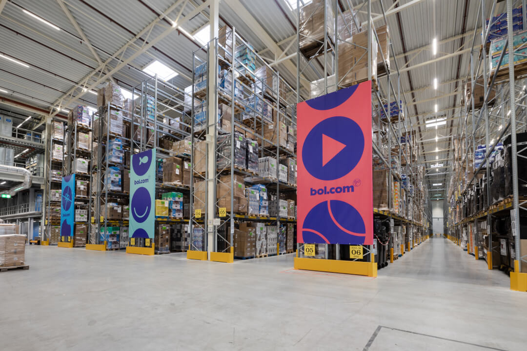 A well-organized warehouse interior with shelves stocked with products, featuring the bol.com brand. Ideal for logistics or e-commerce.