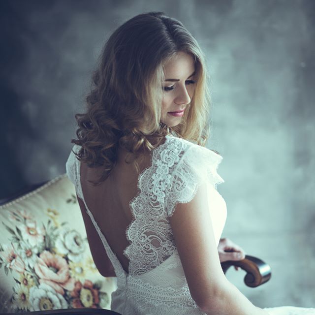 A woman with blonde hair wearing a lace dress looks down. The soft lighting creates a dreamy and sensual mood.