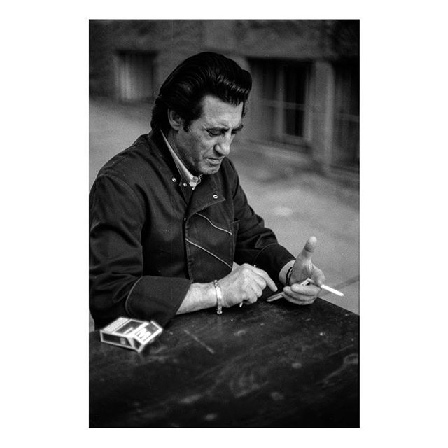 A man sits smoking, captured in a timeless black and white portrait reflecting on a moment of contemplation.