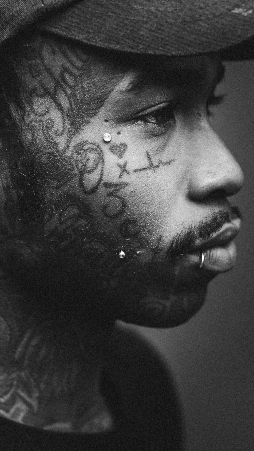 Striking black and white portrait of a man with intricate face tattoos and piercings.
