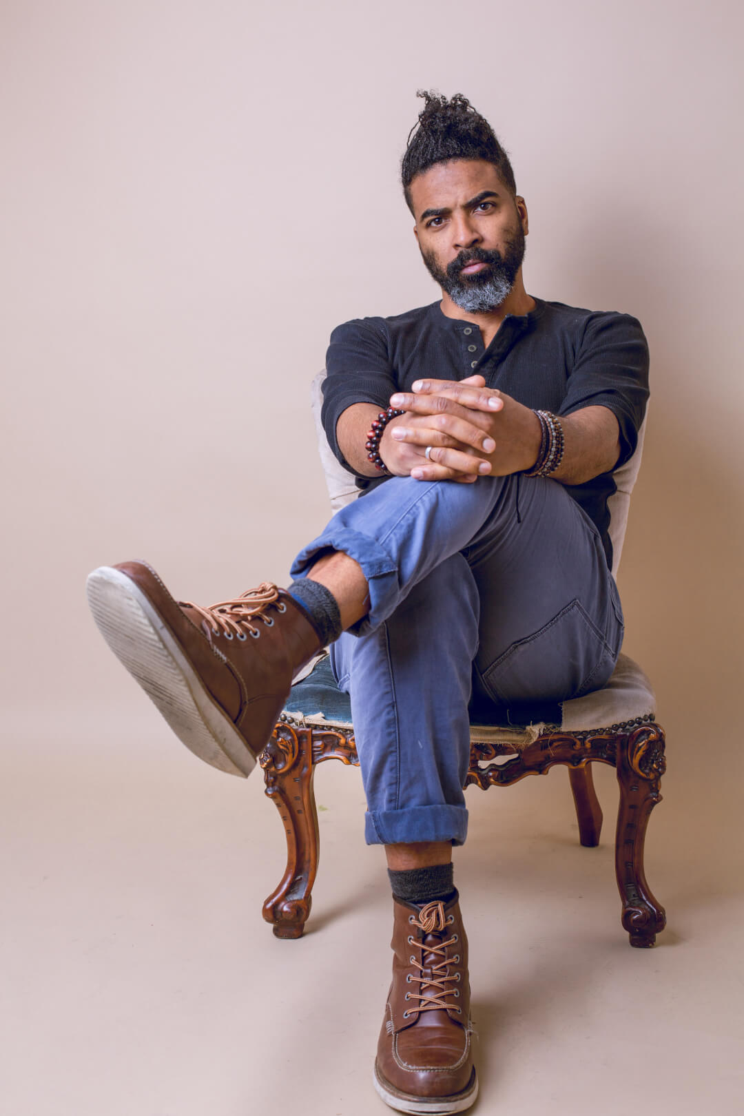 A confident man with a beard sits in a chair, posing for an editorial portrait in a studio.