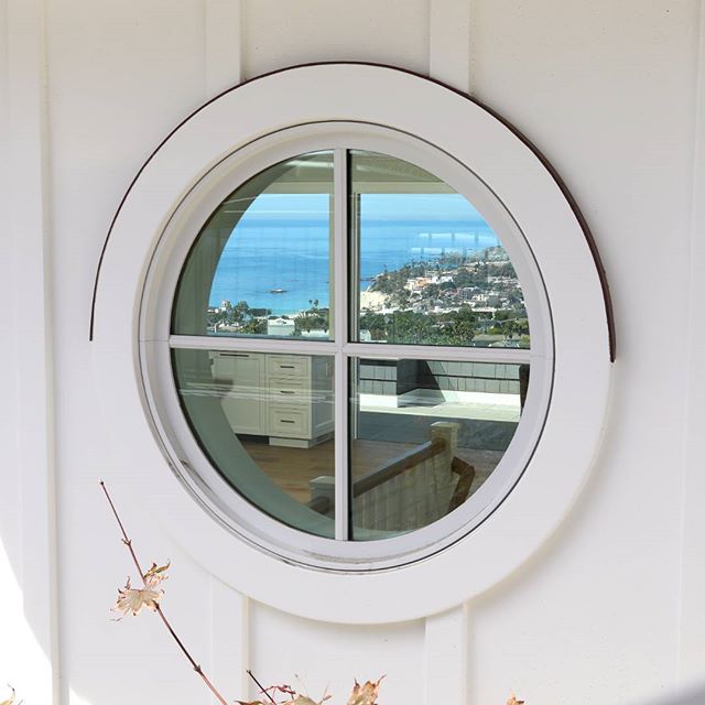 A round window reflects a serene ocean view and a glimpse of a modern interior, blending indoor comfort with coastal charm.
