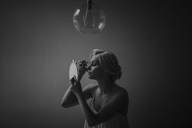 A woman applies makeup using a mirror in a softly lit, elegant setting.
