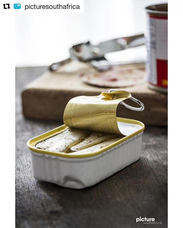 A close-up shot of an opened can of sardines, showcasing the canned food on a wooden surface.