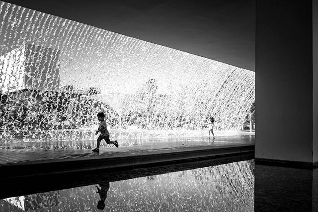 A black and white shot of a young boy running by a waterfall in an urban environment.