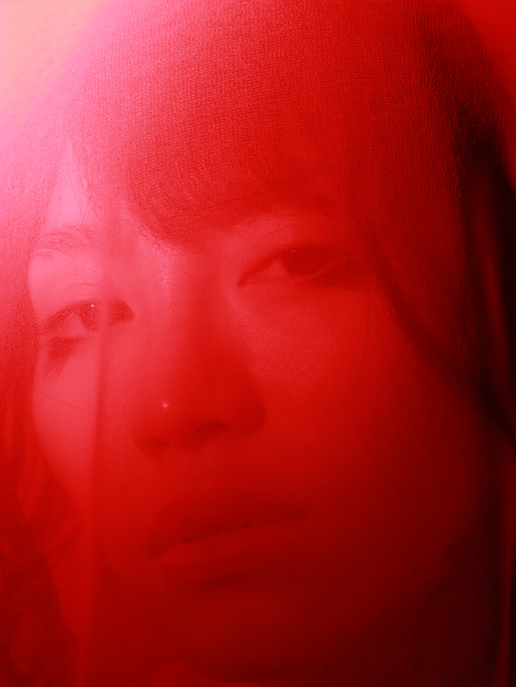 A close-up of a woman's face bathed in red light, creating a moody and intense atmosphere.