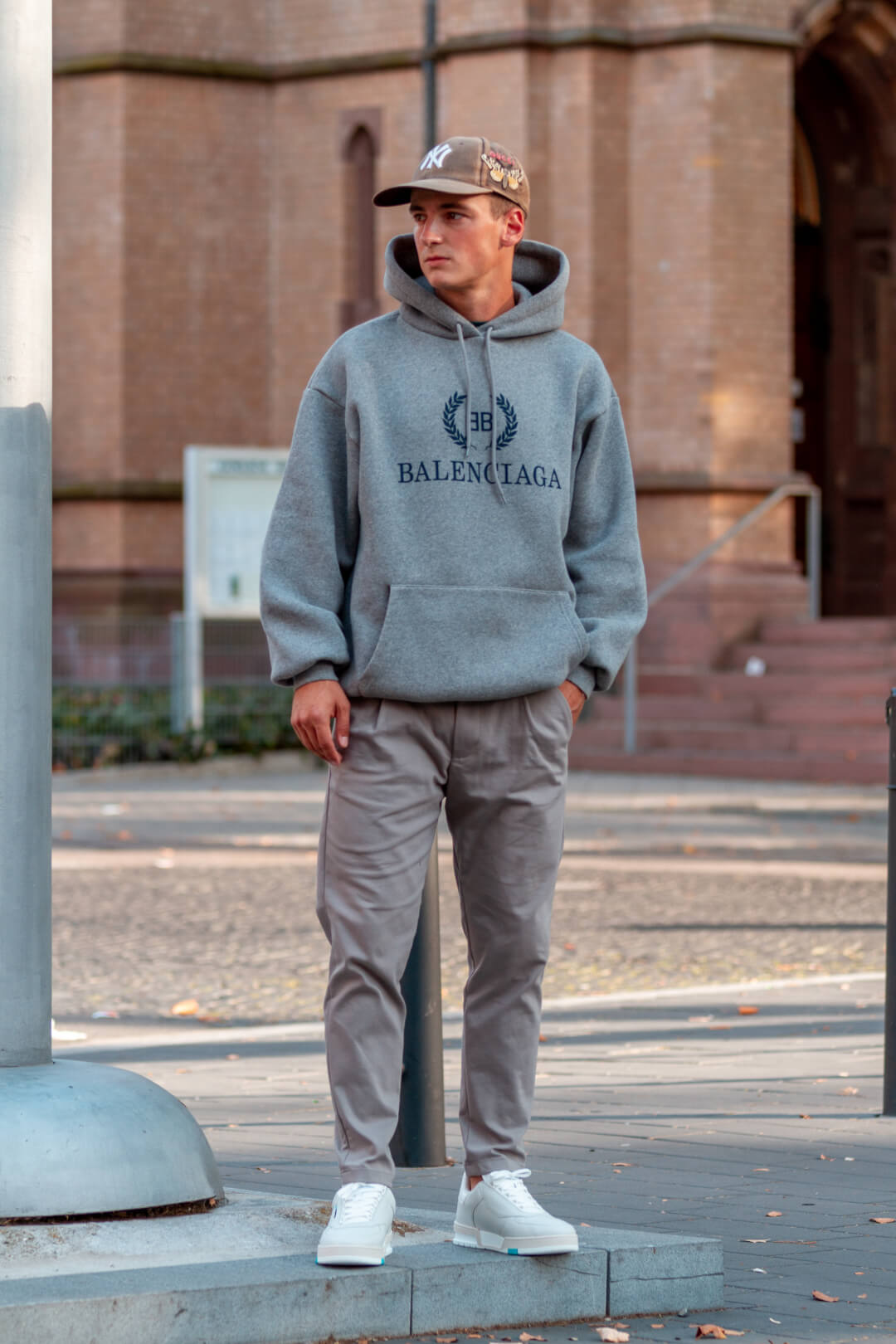 A man in a Balenciaga hoodie, pants, and sneakers stands on a city street.