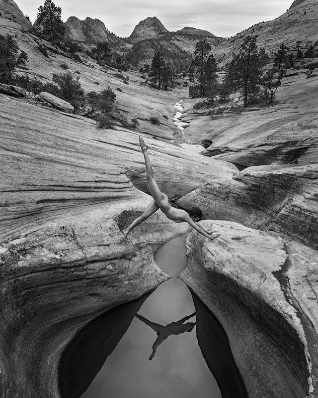 A nude woman poses in a yoga pose over a reflective pool in a canyon landscape, emphasizing balance and connection with nature.