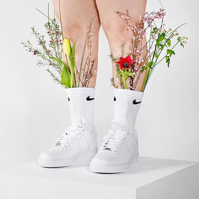 Creative studio shot showcasing legs adorned with flower-filled Nike socks and matching sneakers on a white background.