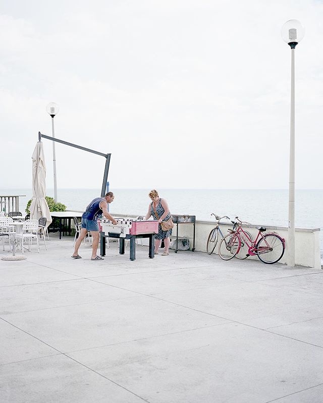 A man and woman play foosball near the ocean on a sunny day with bicycles nearby.