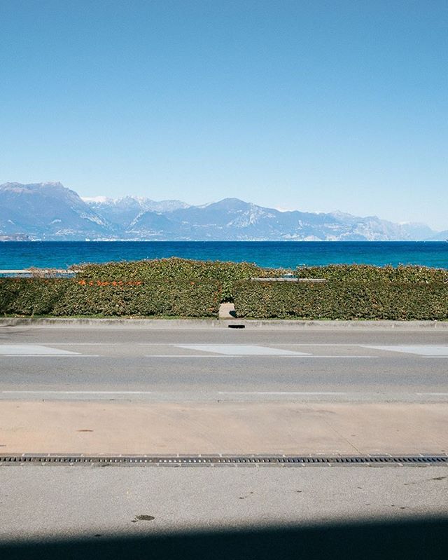 Scenic view of a road by the sea, with mountains in the background under a clear blue sky.
