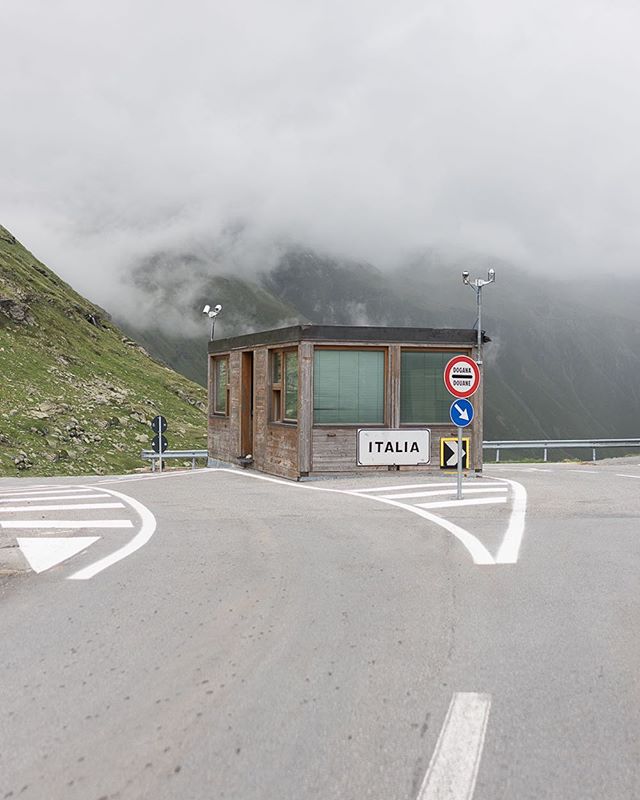 A quiet border crossing station in Italy, nestled in a mountain pass under a cloudy sky.