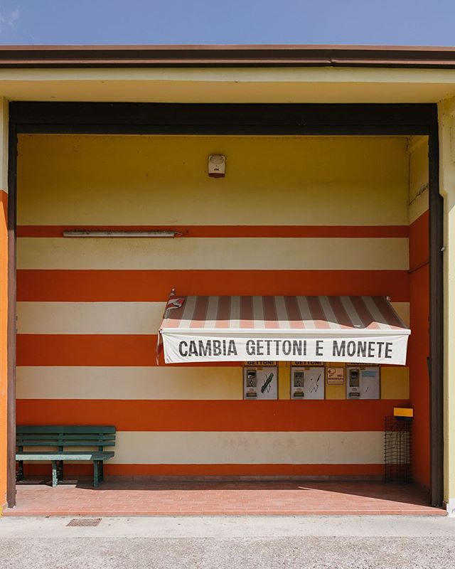 A yellow and orange striped building with a bench and ticket machines under an awning.