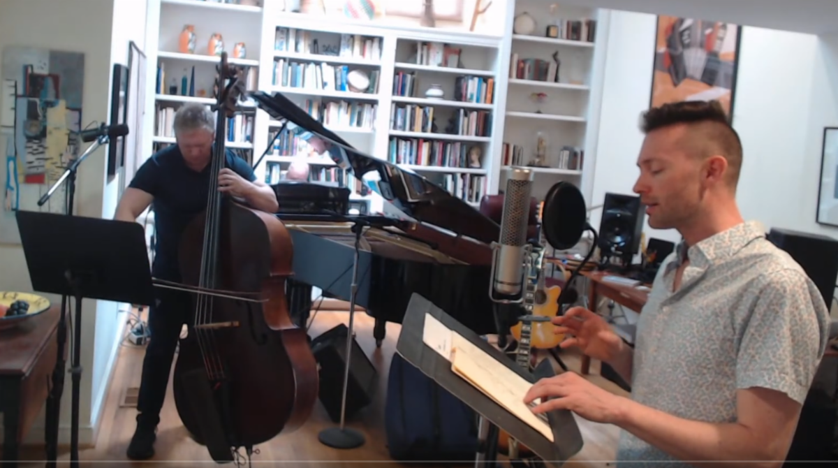 Three musicians in a home music studio that features a grand piano and built-in bookcases in the background.