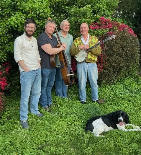 The men of Barnstorm lined up in front of some tall flowering bushes, with a black-and-white dog at their feet