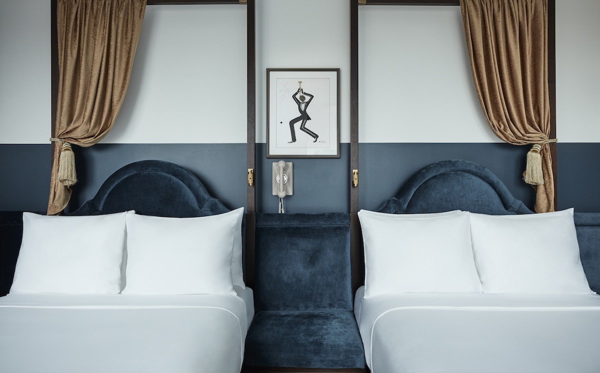 A hotel room with two beds, white pillows, and blue headboards.