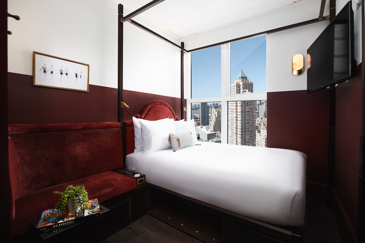 A hotel room with a four-poster bed, red couch, and city view.