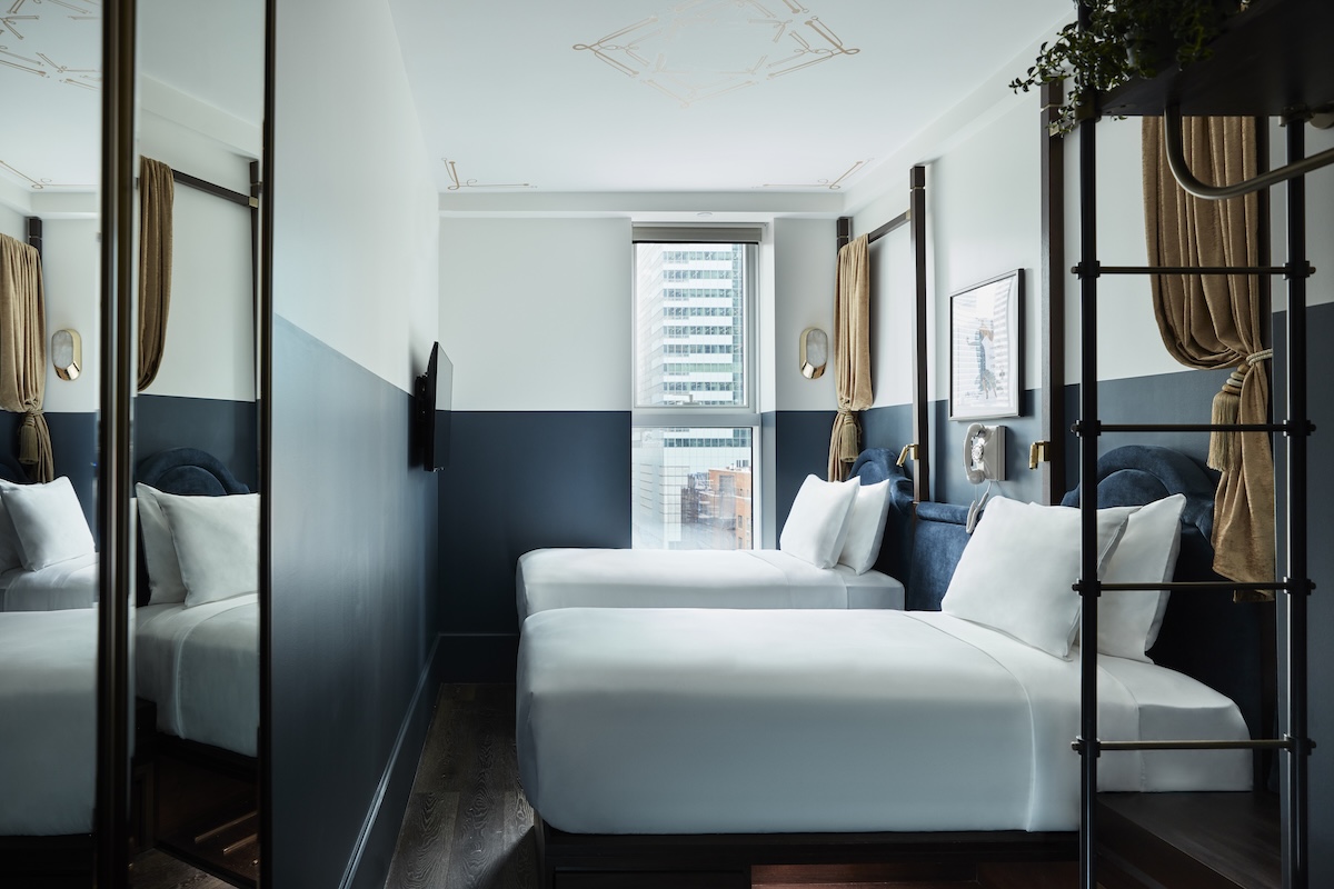 A hotel room with two twin beds, a window, and a mirror.