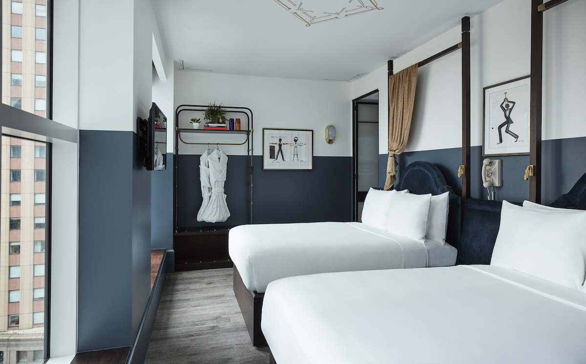 A hotel room with two beds, a window, artwork, a desk, and a TV.
