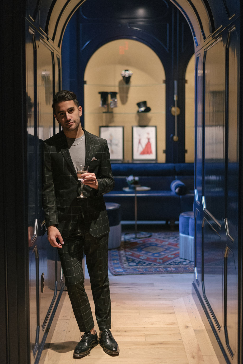 A man in a suit standing in an open doorway leading to a lounge area with a couch and coffee table.