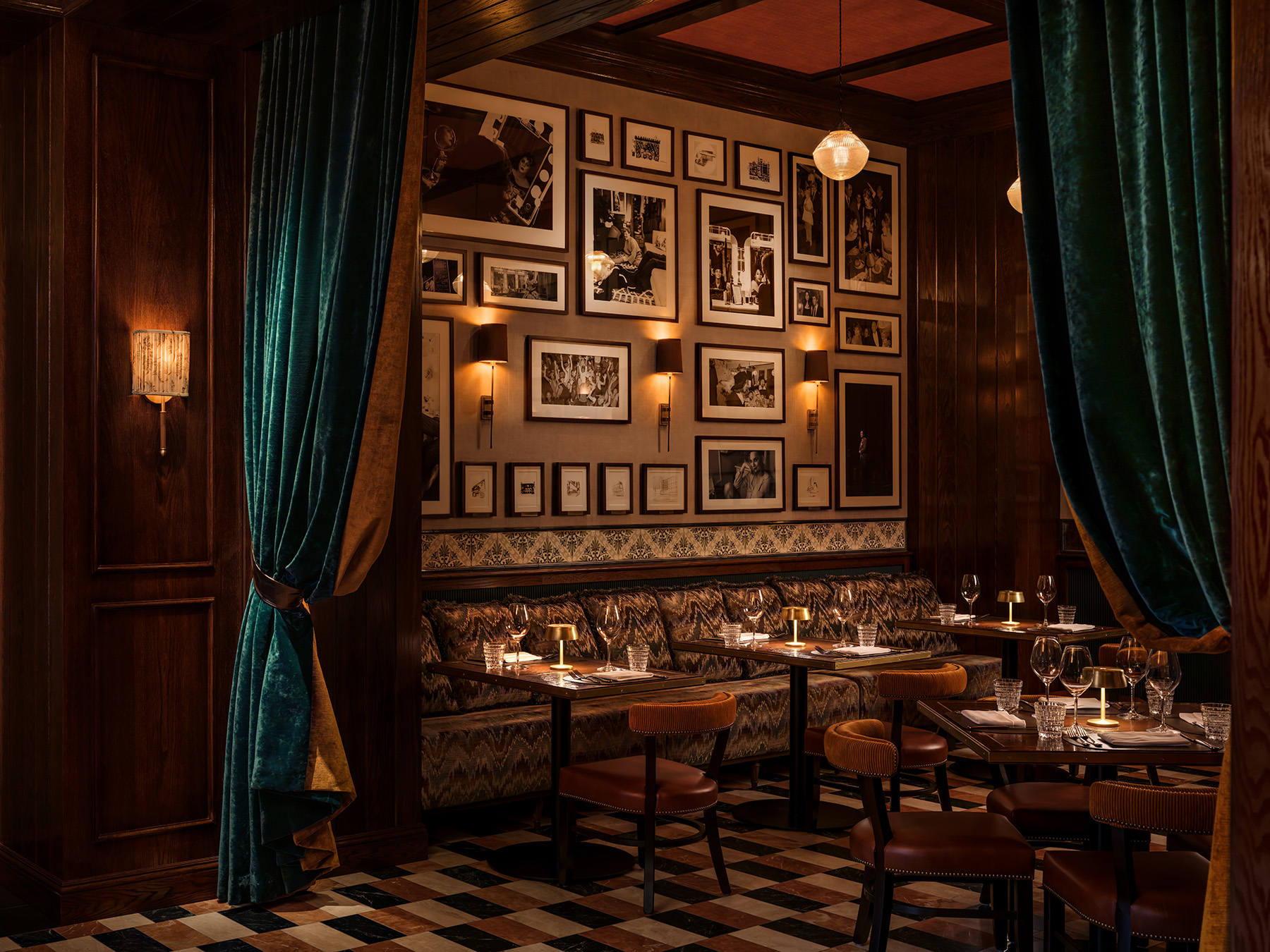A dimly lit dining area with booth seating, tables, and chairs, adorned with framed photos on the walls.