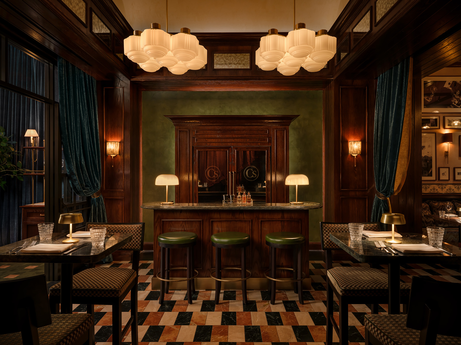 A dimly lit bar with a green and brown color scheme, featuring a bar counter with stools, tables with chairs, and decorative lighting.