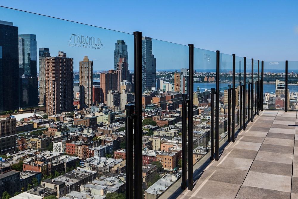 A rooftop bar with a glass railing overlooking the city skyline