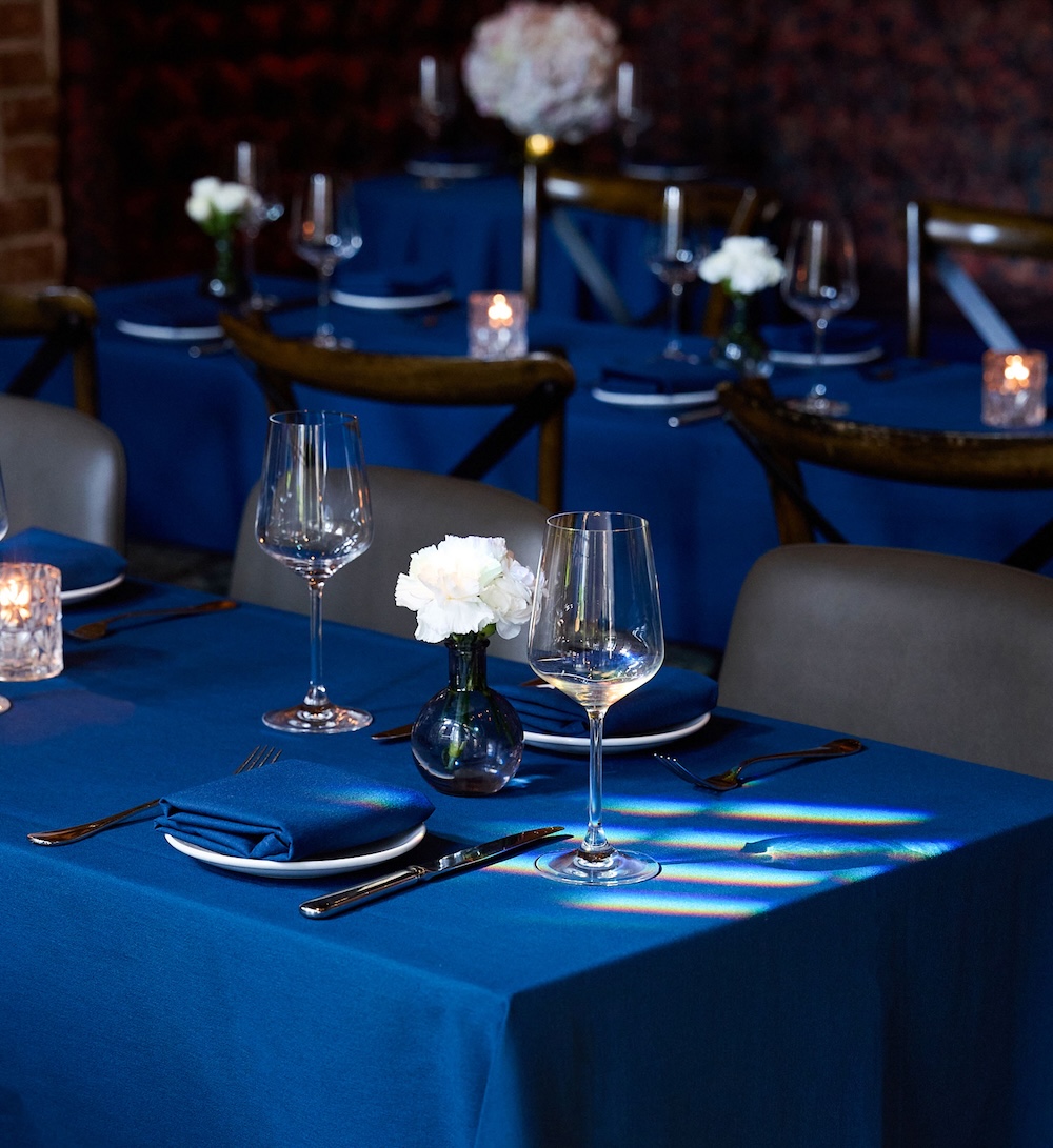 A formal dining area with blue tablecloths, white flowers, and candles