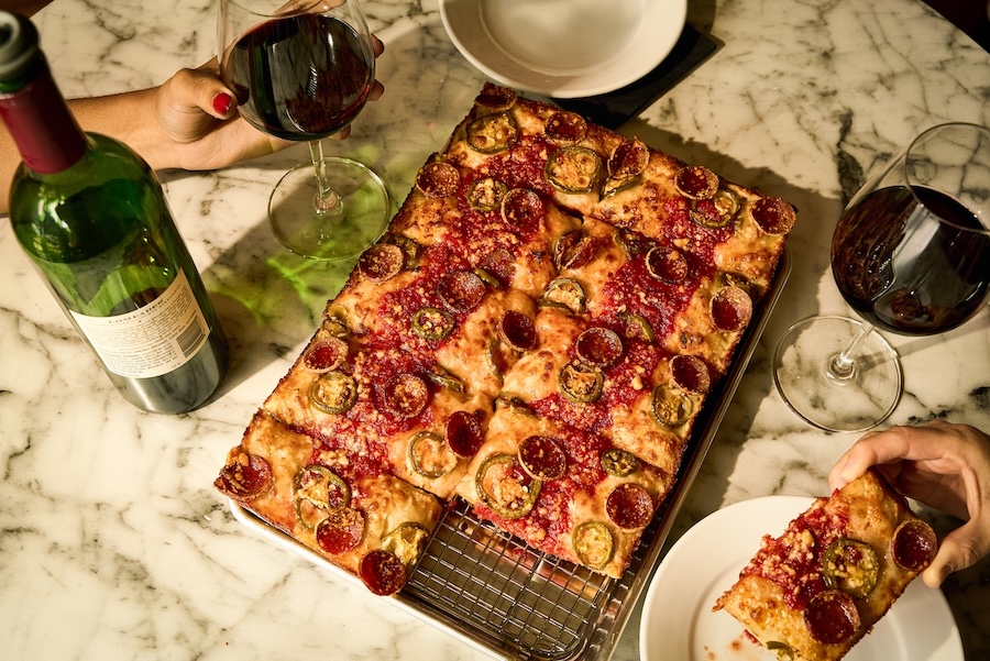 A pizza with pepperoni and jalapenos on a marble table with wine