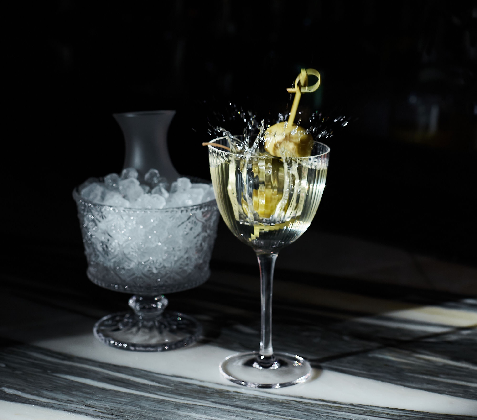 a glass of champagne with a splash of liquid and a lemon twist next to a bowl of ice