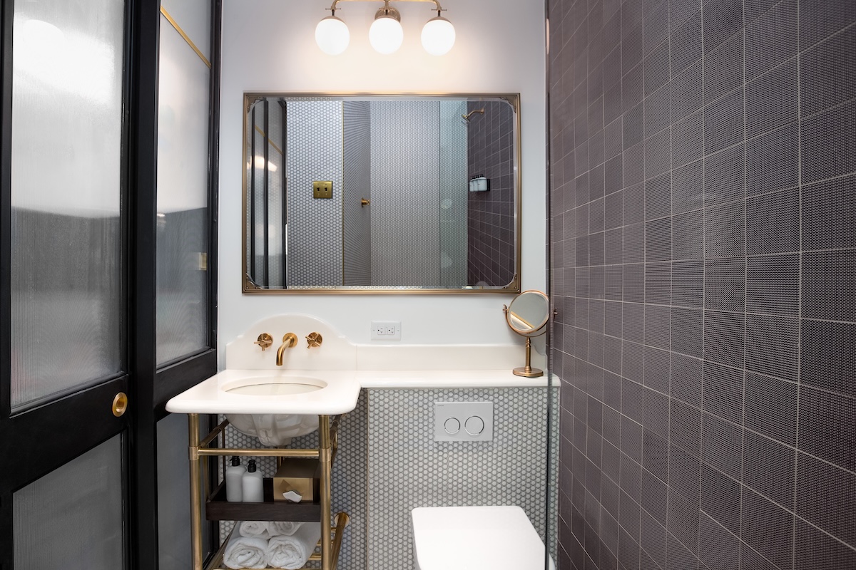 A bathroom with a white sink, gold fixtures, and gray tiles on the walls.