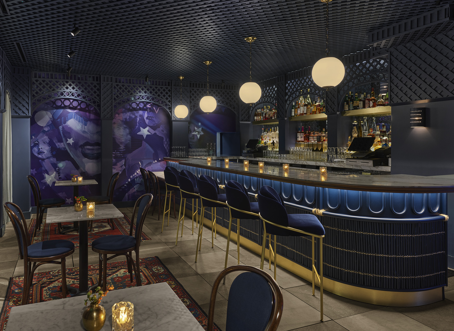 A bar with a blue and gold color scheme, shelves of alcohol, and several tables with chairs.