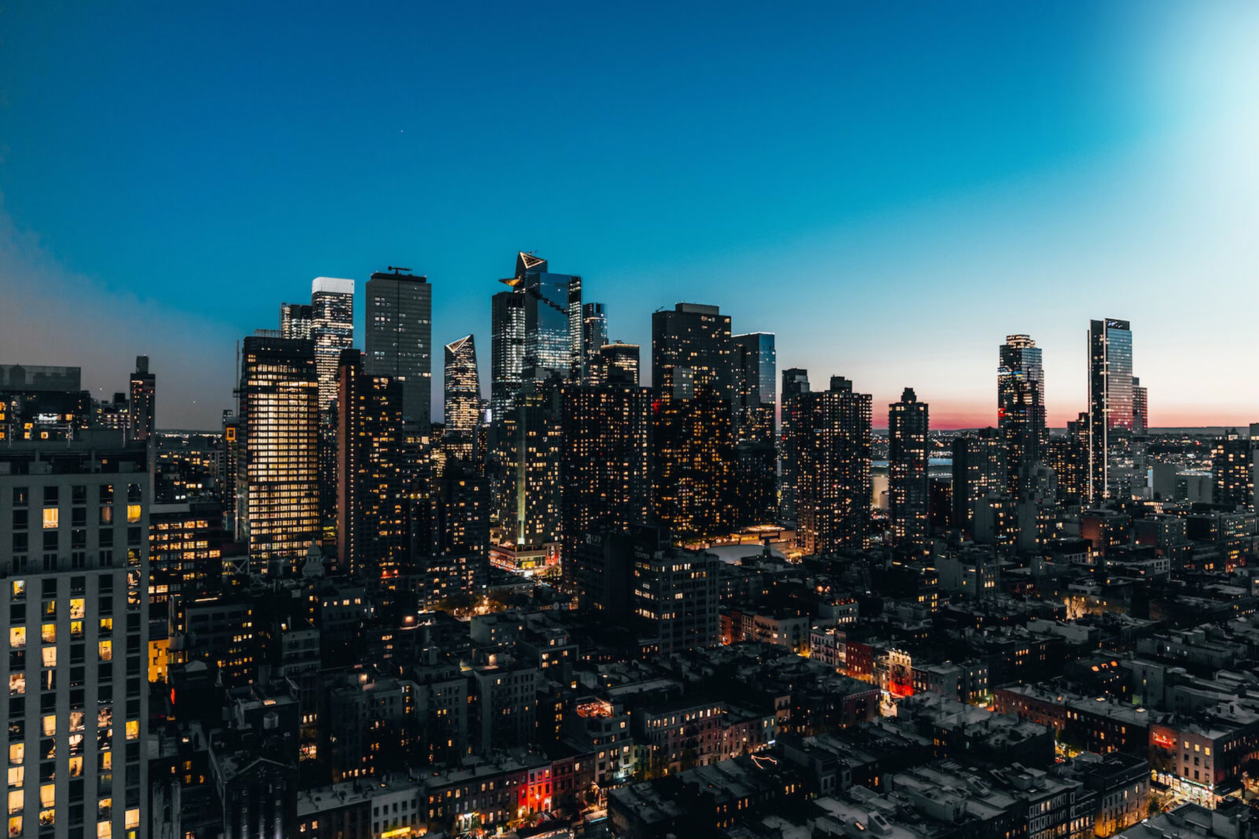 A city skyline at dusk with many lit skyscrapers.