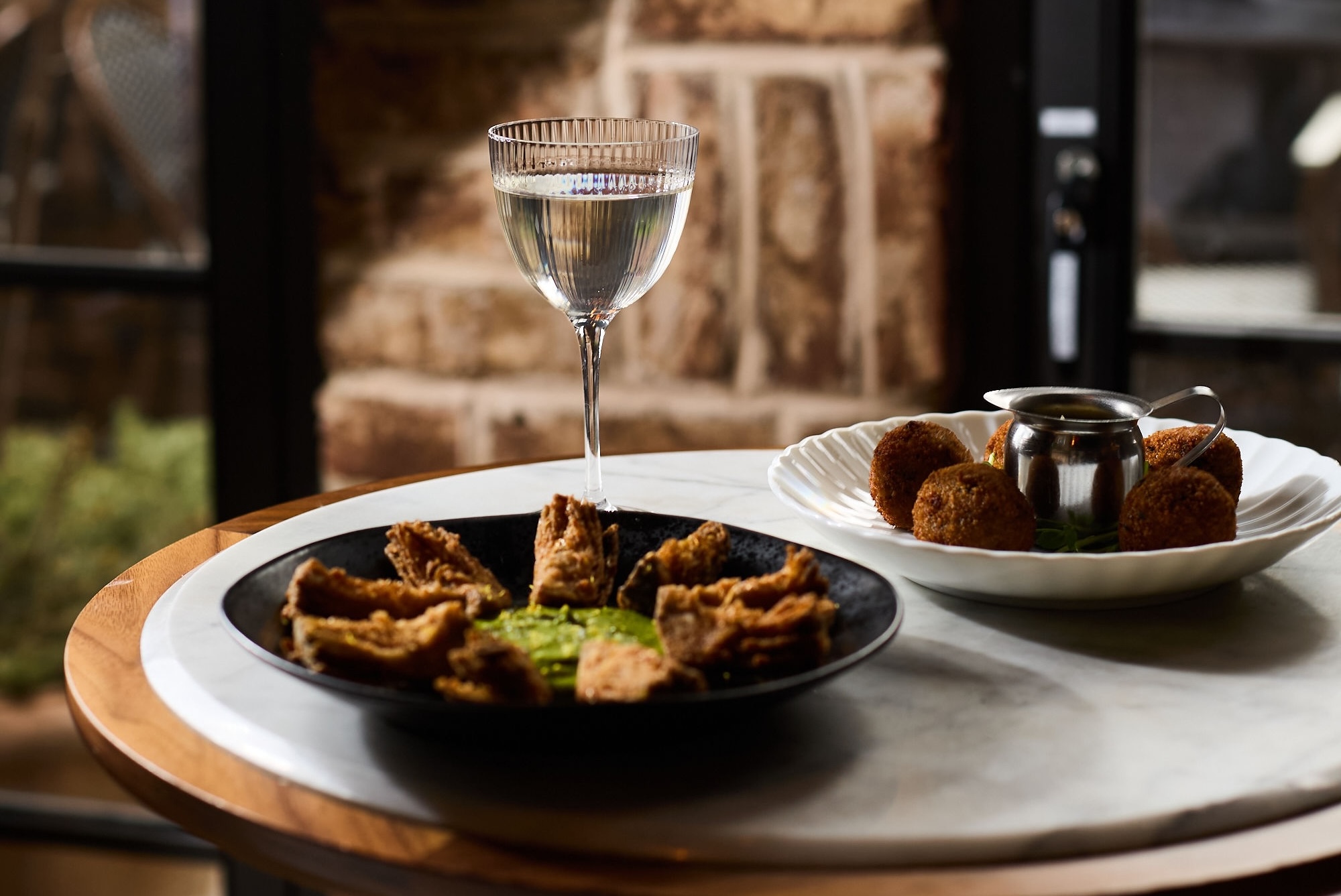 a table with a plate of fried food and a glass of white wine