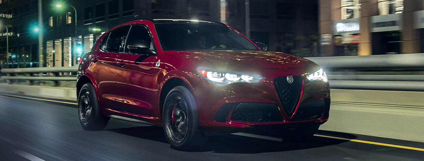 Front side view of a red 2025 Alfa Romeo Stelvio driving in the city