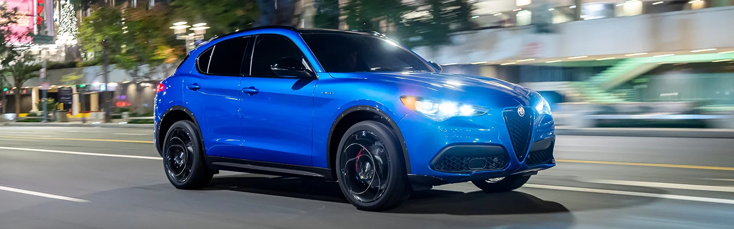 Side view of a blue 2025 Alfa Romeo Stelvio driving in the city