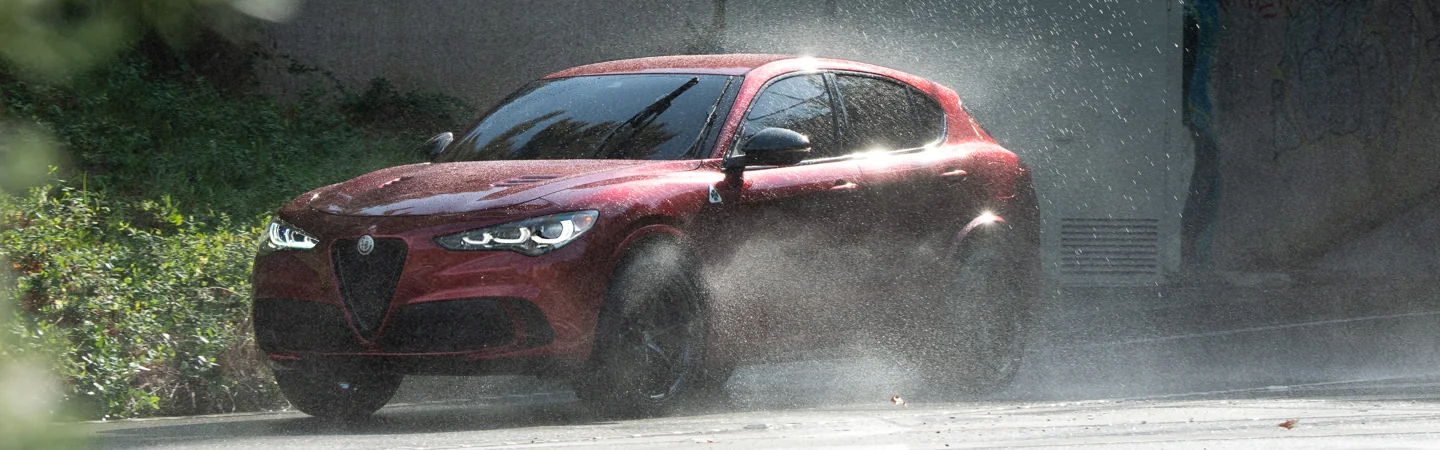 Front side view of a red 2025 Alfa Romeo Stelvio driving in the rain